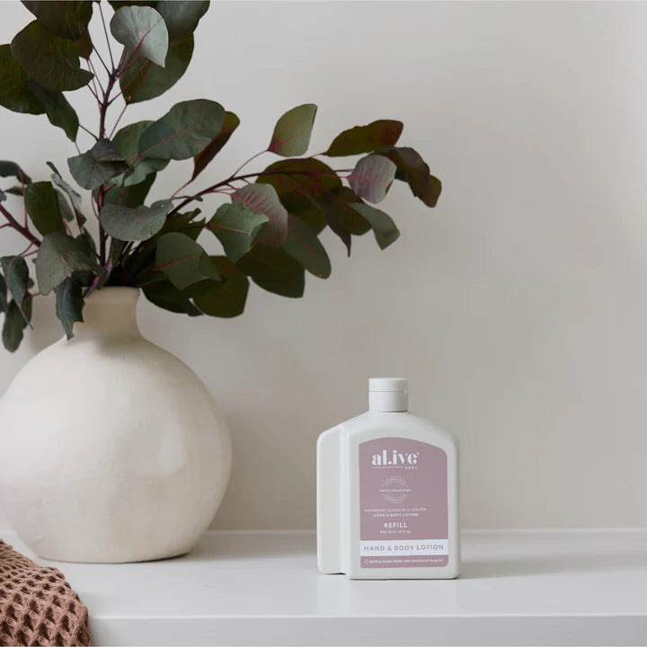 White bottle of a'live lotion on a white surface with a vase and branches in the background.