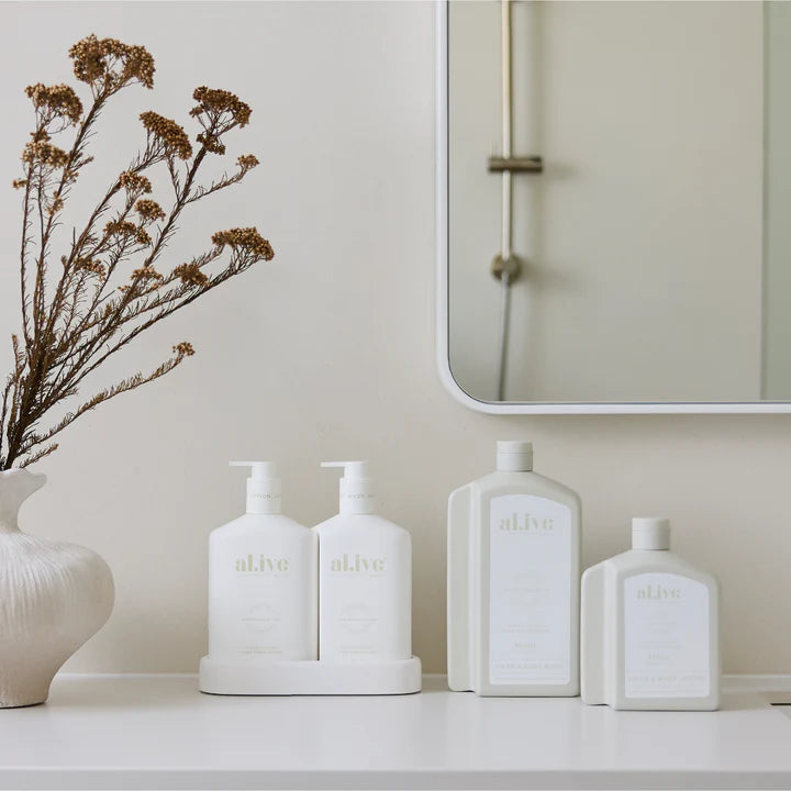 White ceramic bottles with 'al.ive' branding on a shelf against a neutral wall.