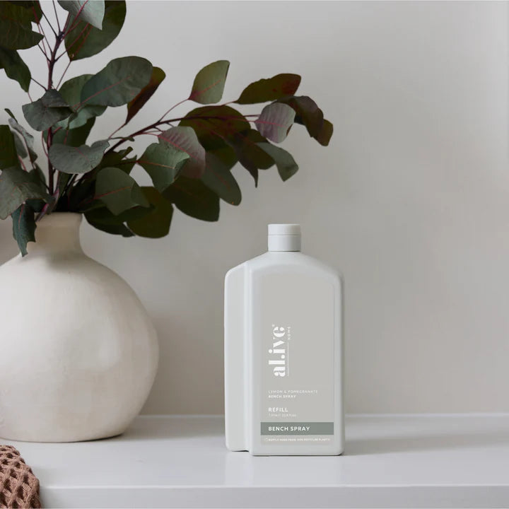 White bottle labeled 'alive' on a shelf with a vase and plant