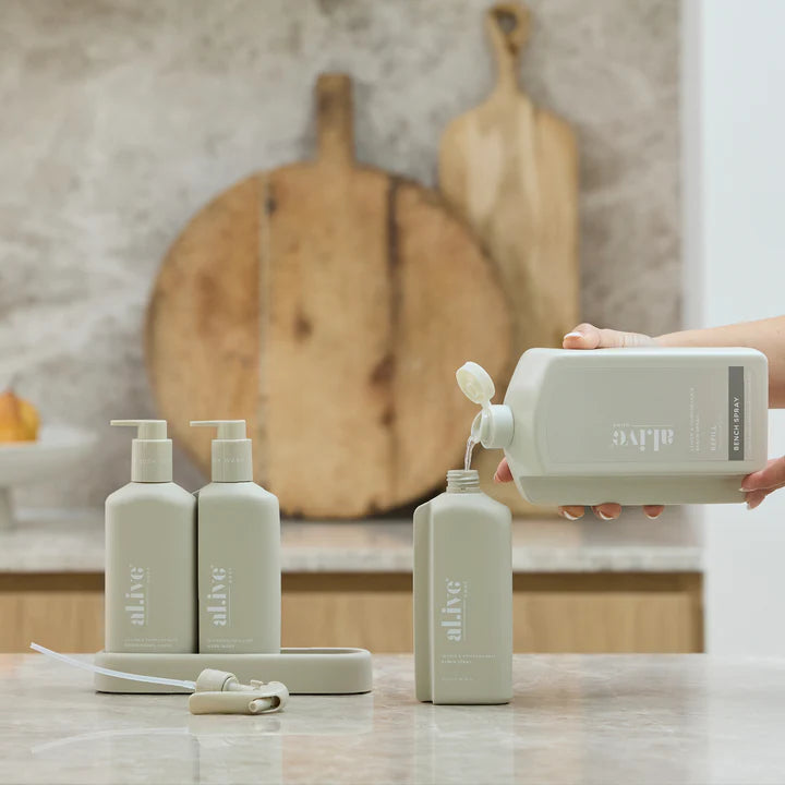 Person pouring liquid from a large bottle into smaller bottles on a kitchen counter.