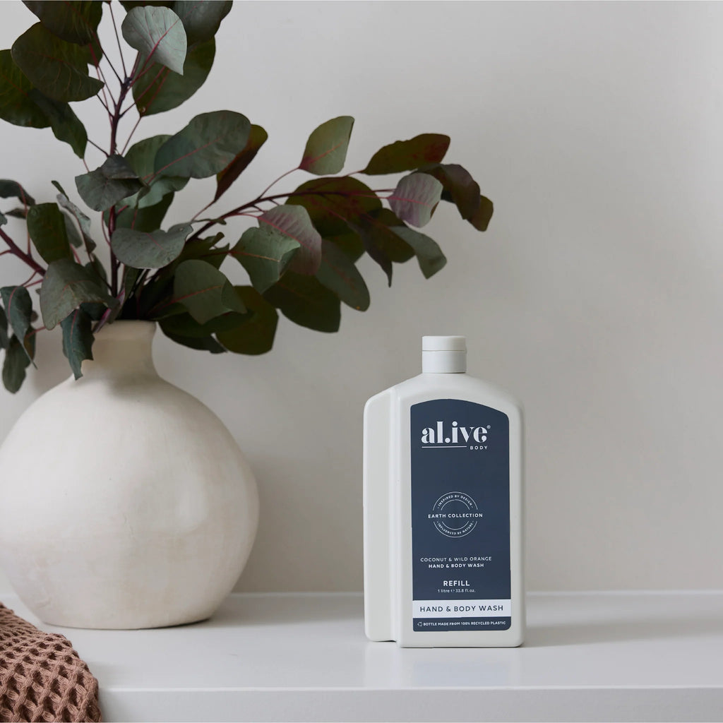 White bottle of 'alive' hand and body wash on a shelf with a vase and plant in the background.