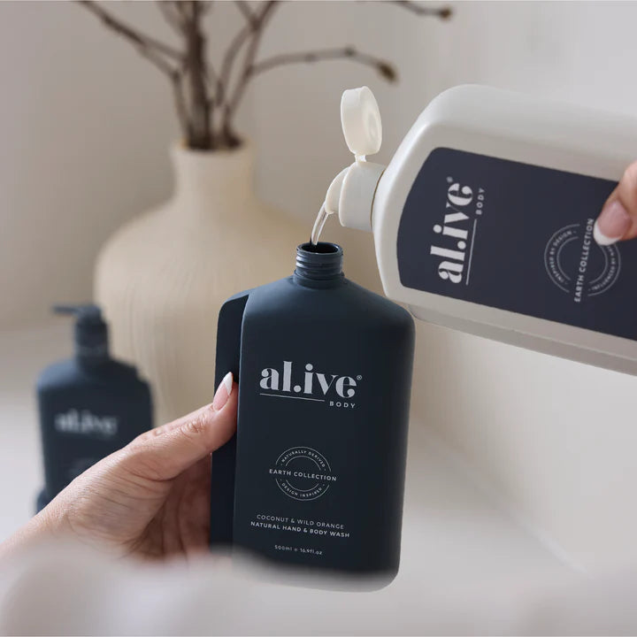 Person pouring body wash from a white bottle into a black 'al.i.v.e' bottle on a neutral background.