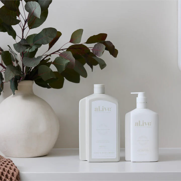 Two white bottles with 'alive' branding on a shelf next to a vase with green leaves.