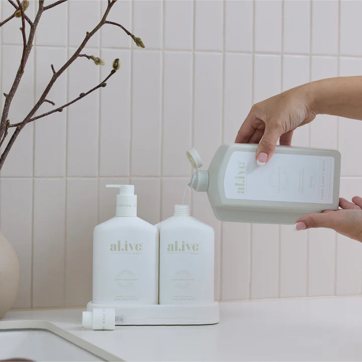 Person pouring liquid from a container labeled 'alive' into a bottle on a bathroom counter.