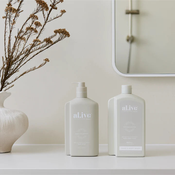 Two 'alive' bottles on a white surface with a mirror and vase in the background.