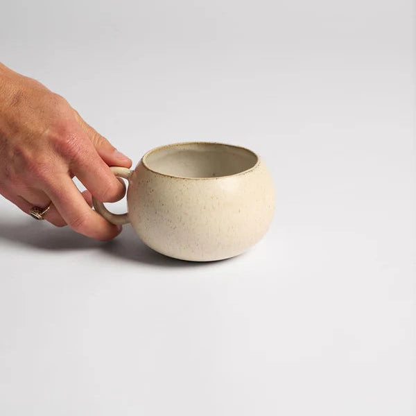 Hand holding a beige ceramic cup on a light gray background