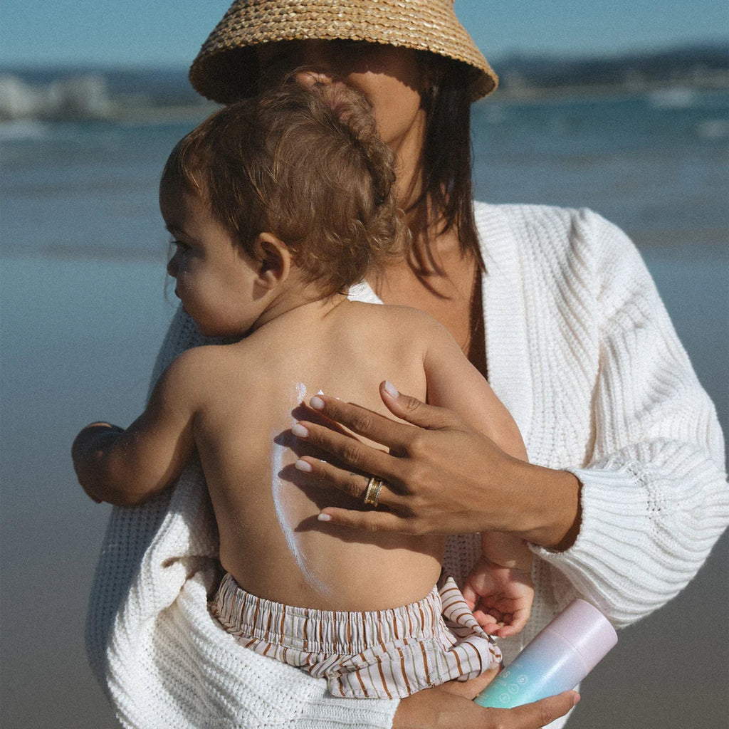 Woman applying sunscreen to a child's back on a beach