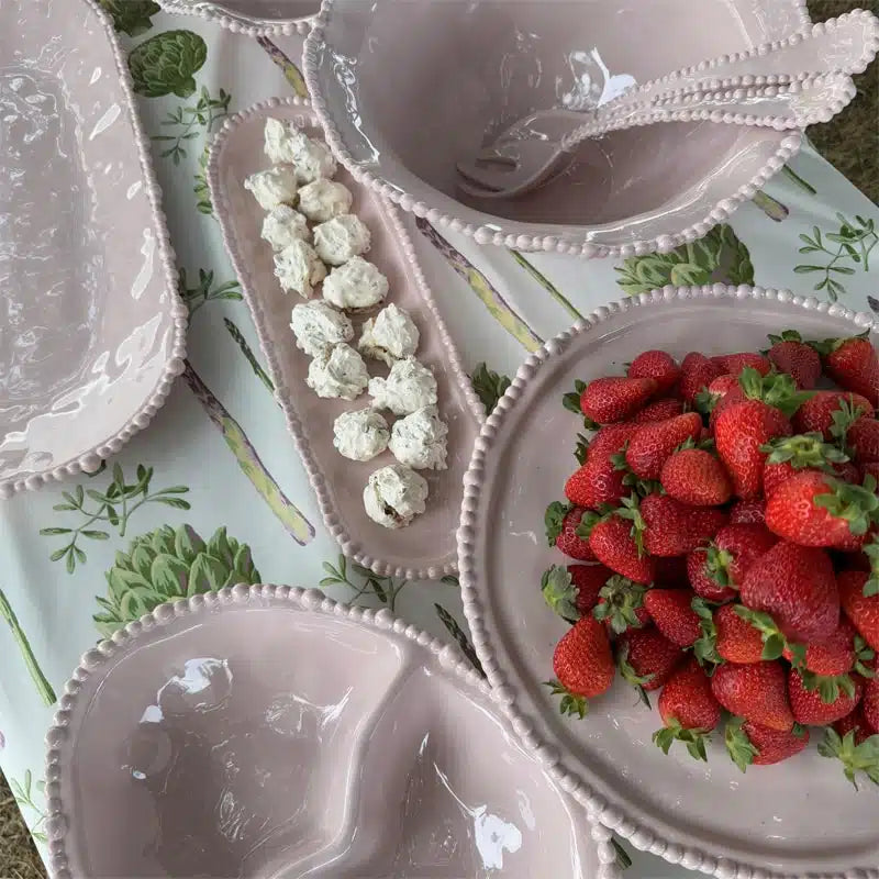 Pink melamine plates with strawberries and cauliflower on a patterned tablecloth.