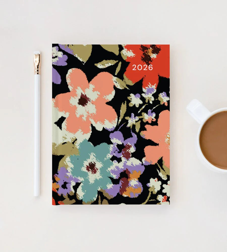 Floral-patterned notebook with '2026' on a white surface next to a pen and mug.