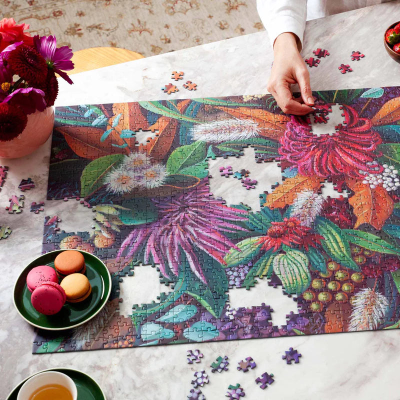 Person working on a colorful puzzle with flowers and plants on a table.