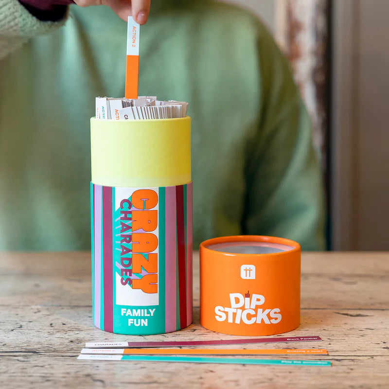 Colorful containers with 'Charades' and 'Dip Sticks' branding on a wooden surface.