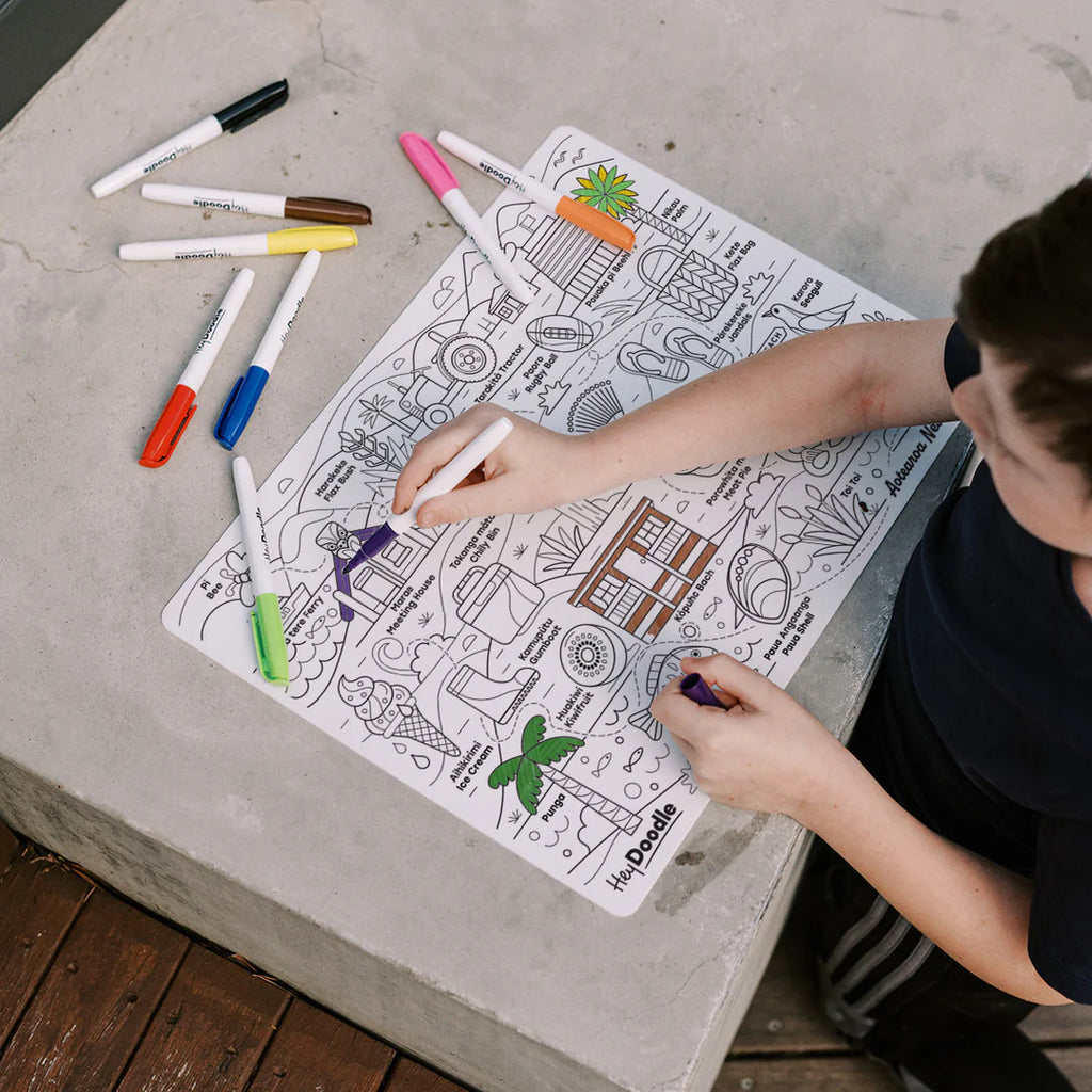 Person coloring a detailed coloring book page with markers on a concrete surface.