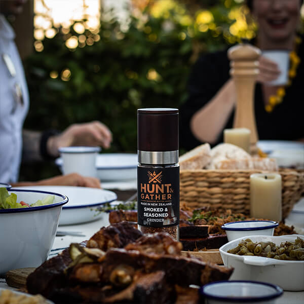 Hunt & Gather seasoning bottle on a table with food and people in the background