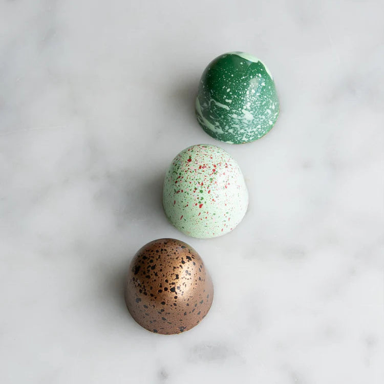 Three chocolate bonbons  in green, white, and bronze on a marble surface
