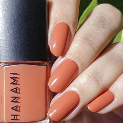 Hand holding a bottle of Hanami nail polish with peach-colored nails.
