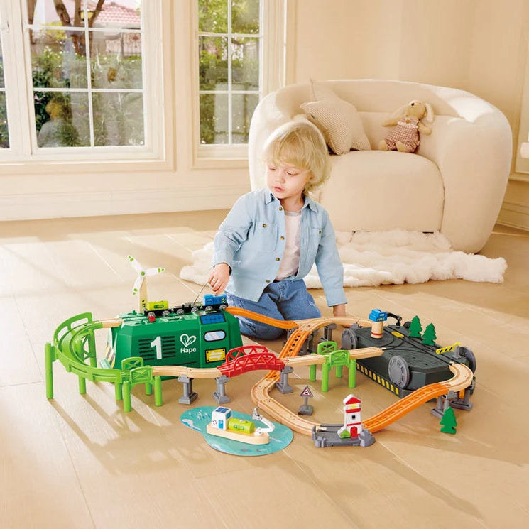 Child playing with a toy train set on a wooden floor in a living room.