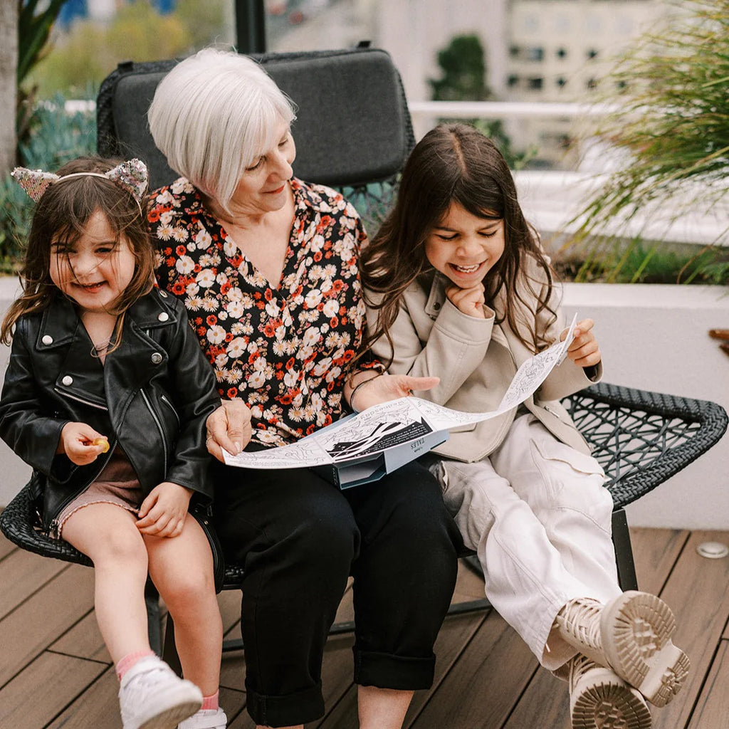 Woman with two young girls sitting outdoors, reading a book together.
