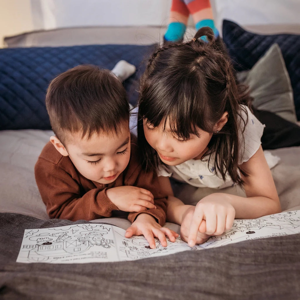 Two children looking at a coloring book on a bed.
