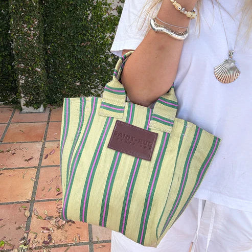 Woman holding a striped bag with a visible brand logo on a tiled floor.