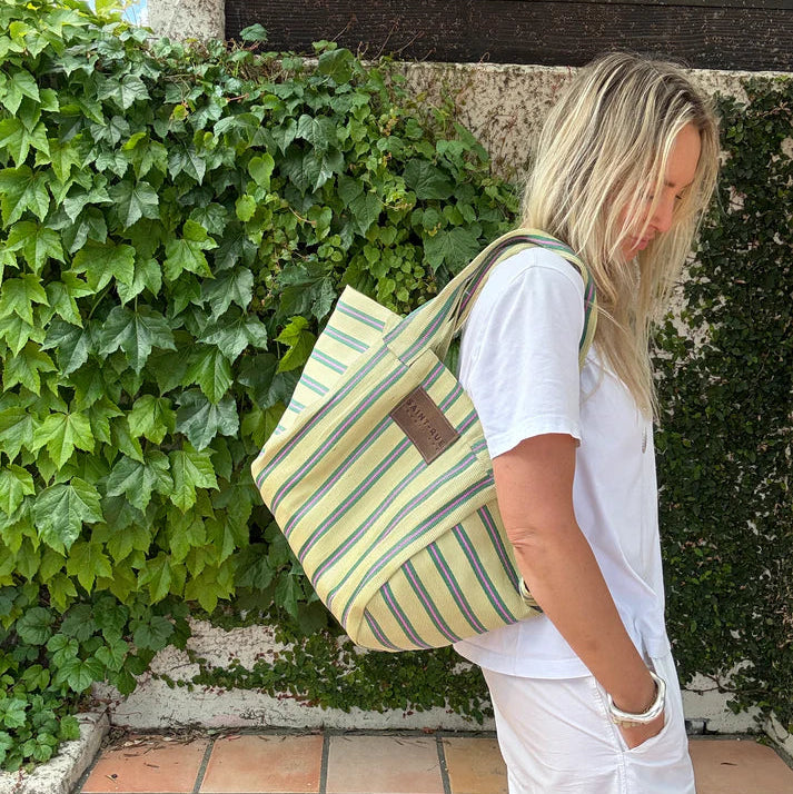 Person wearing a striped tote bag outdoors near greenery