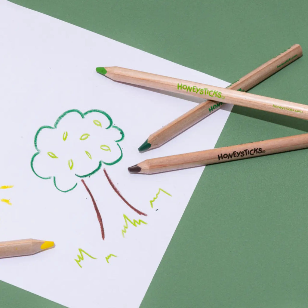 Honeysticks colored pencils on a green background with a child's drawing of a tree.