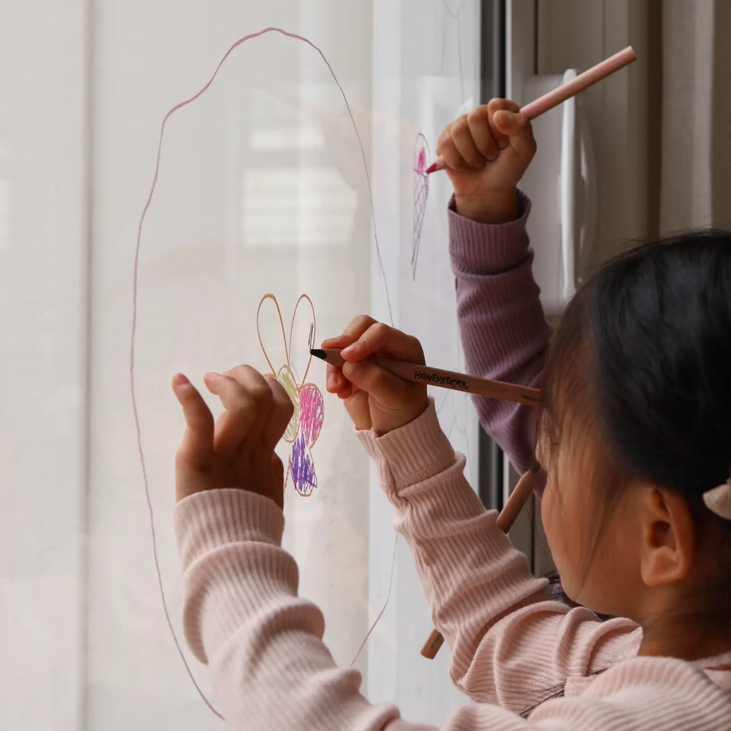 Two children drawing on a window with colorful markers.