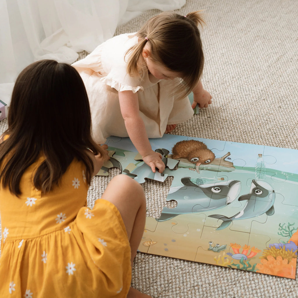Two young girls playing with a puzzle featuring ocean animals on a carpeted floor.