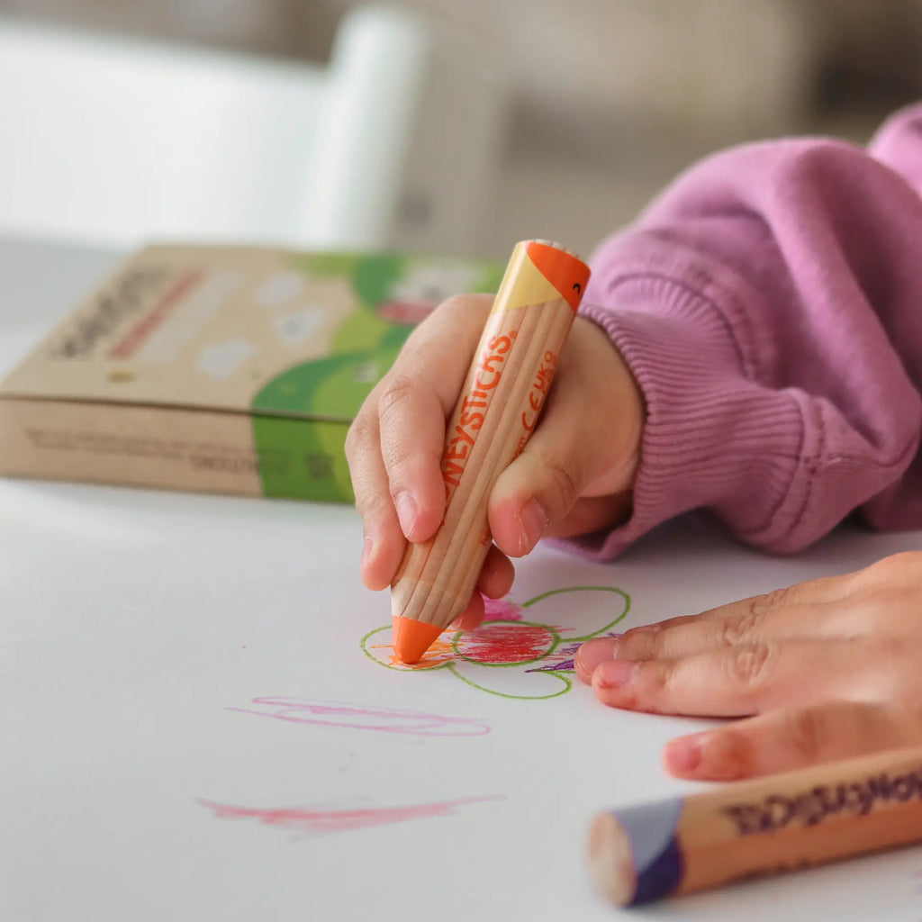 Child's hand holding a Crayola crayon coloring on paper with a book in the background