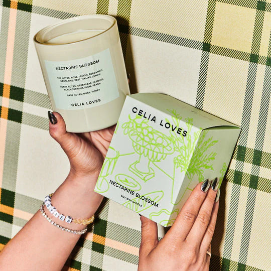 Person holding a Celia Loves Nectarine Blossom candle against a plaid bakcground