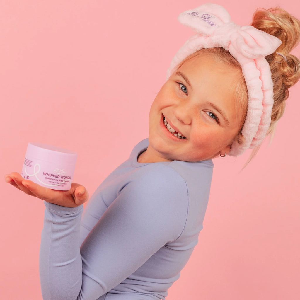 Child wearing bow headband holding a jar against a pink background