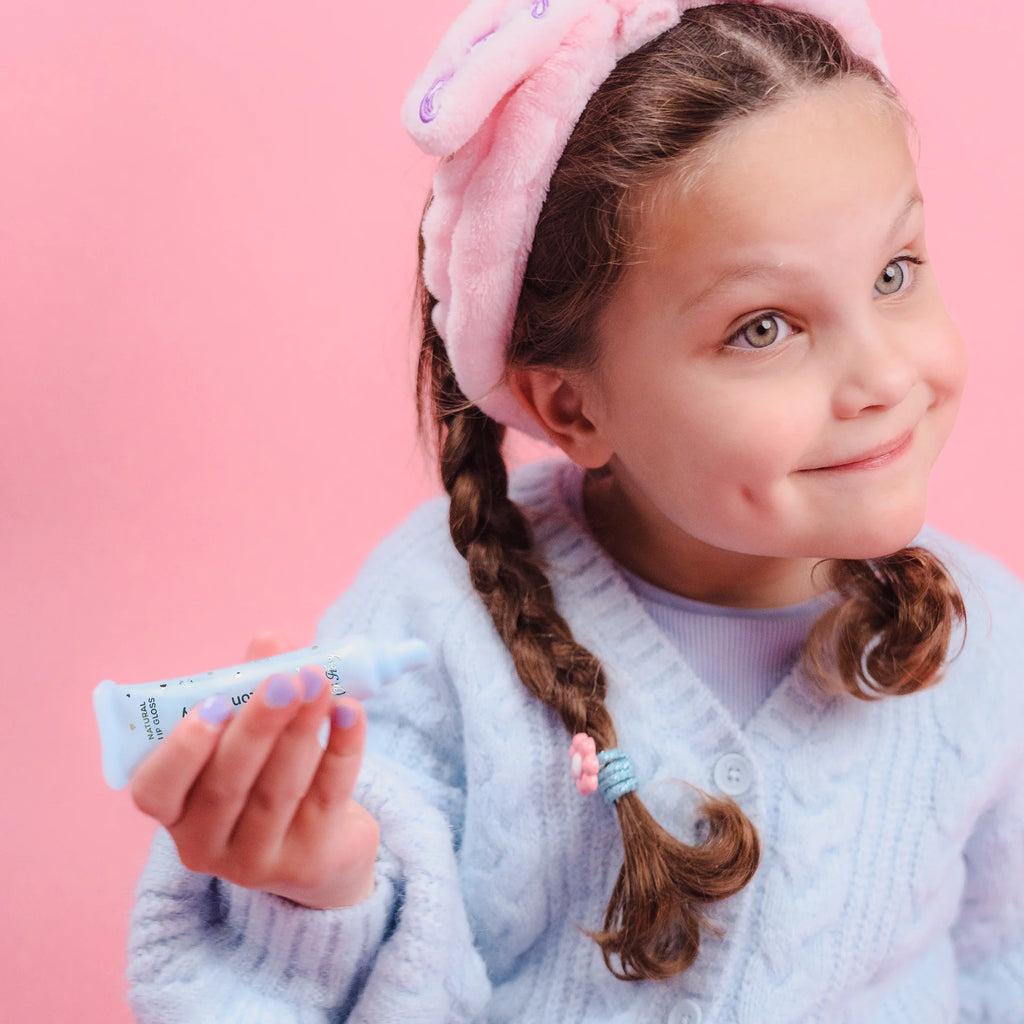 Young girl with braided hair wearing a pink headband against a pink background