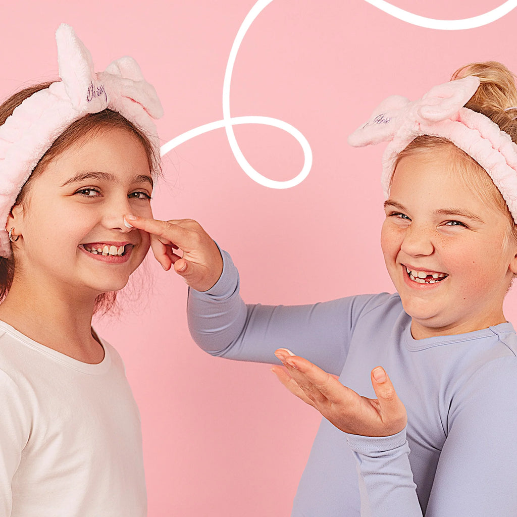 Two children wearing pink bow headbands against a pink background