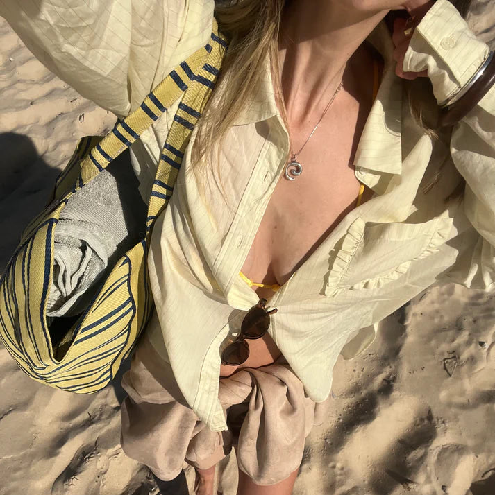 Person in light-colored outfit with a yellow and black bag on a sandy surface