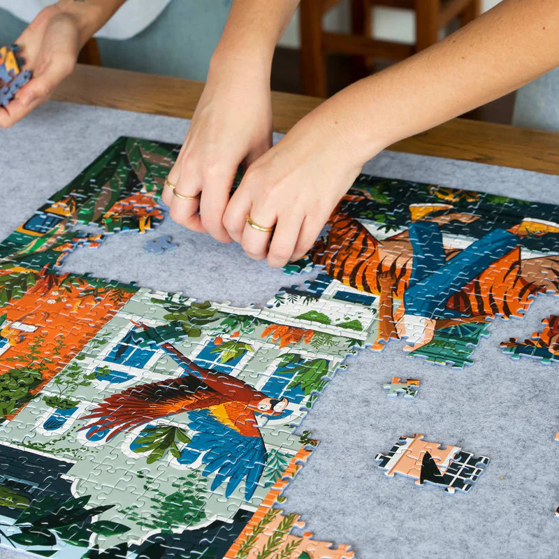 Two people working on a puzzle with colorful animal-themed pieces on a gray surface.