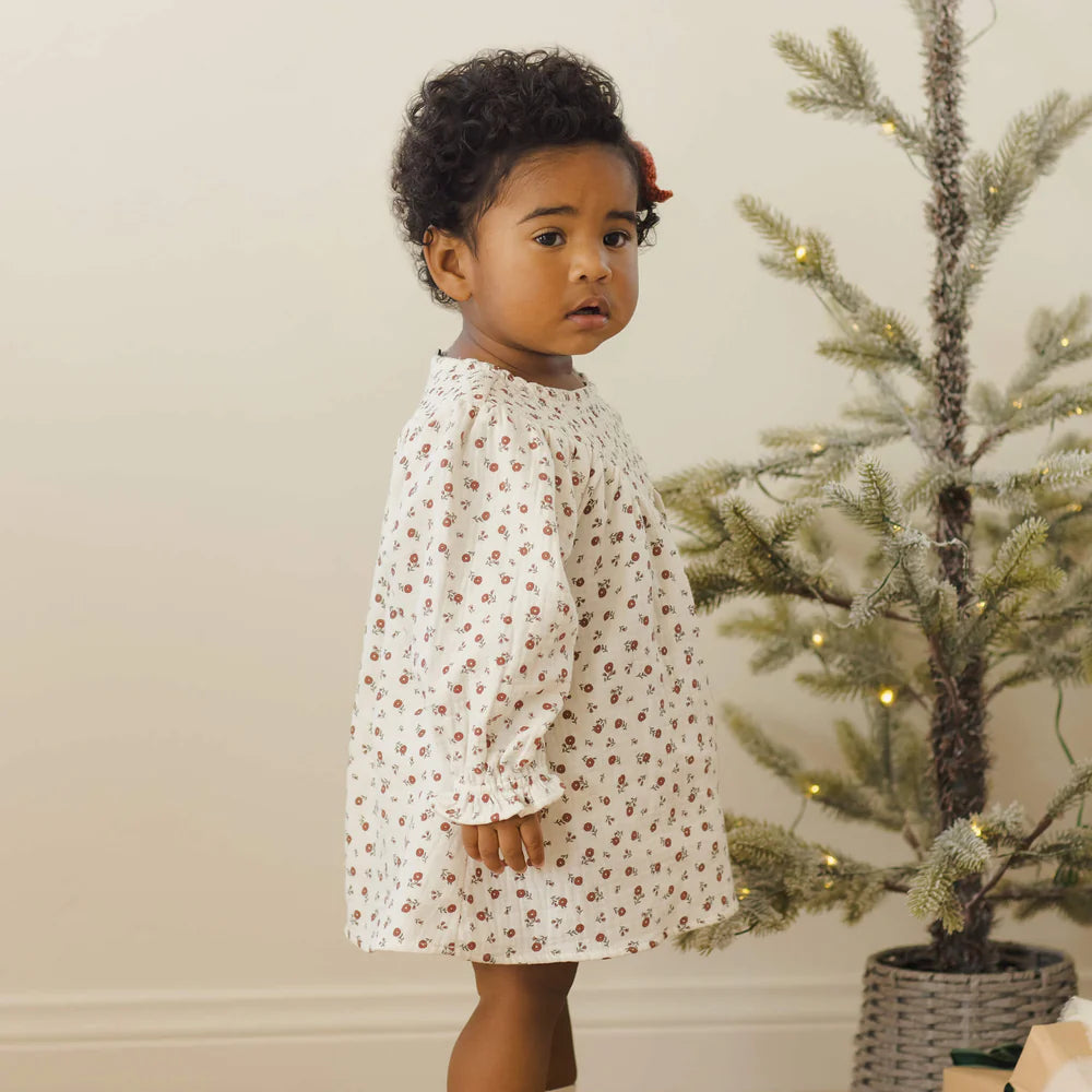 Child in a floral dress standing in front of a decorated Christmas tree.