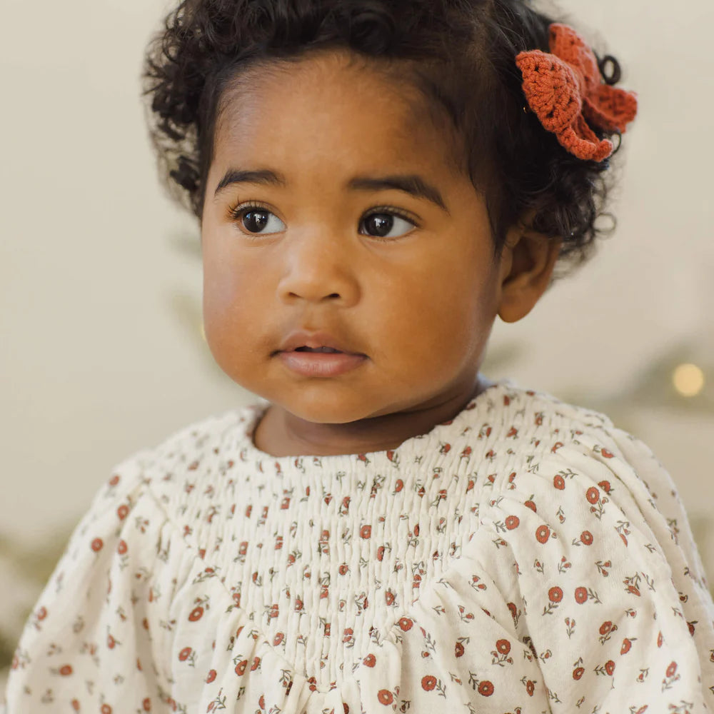 Young child with a floral hair clip wearing a white blouse with small patterns.