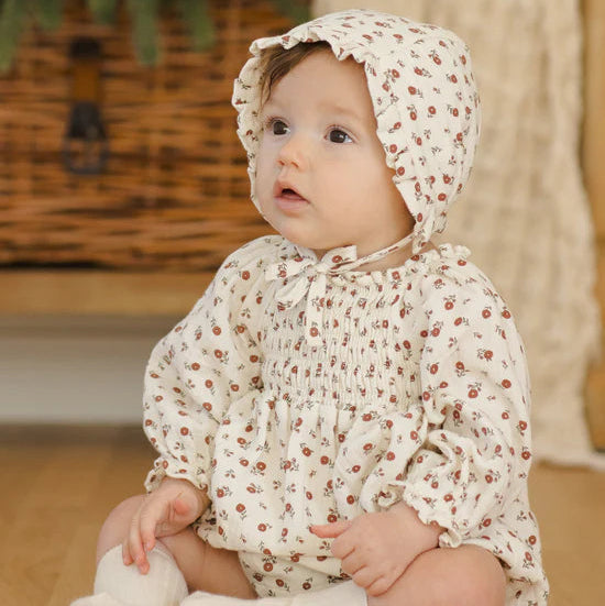 Baby wearing a floral outfit sitting on a wooden floor.