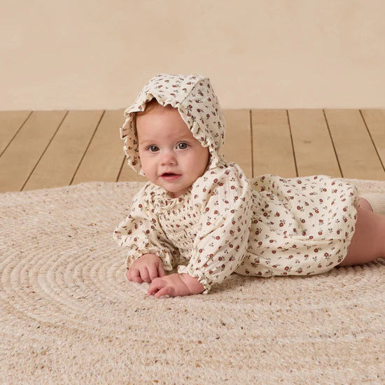 Baby in floral outfit and bonnet lying on a textured blanket