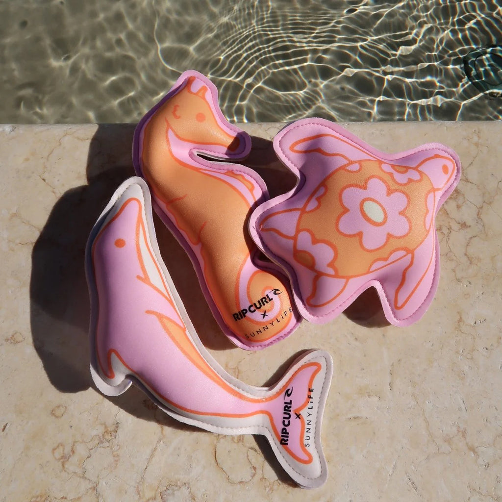 Two colorful shark-shaped pool toys on a stone surface with water in the background