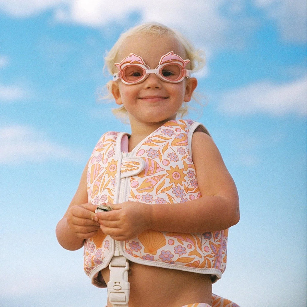 Child wearing a floral life jacket and pink sunglasses against a blue sky.