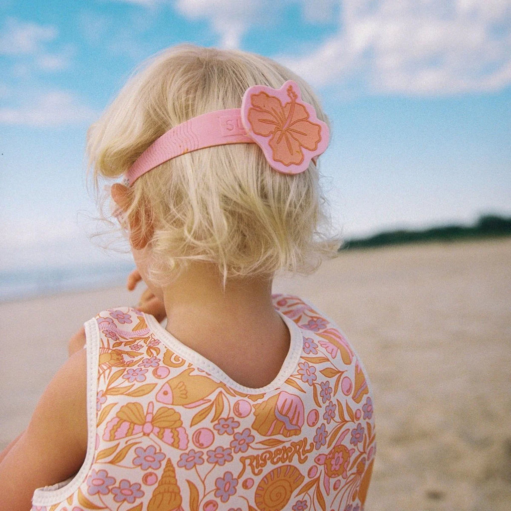 Child wearing a floral-patterned dress and pink headband on a beach