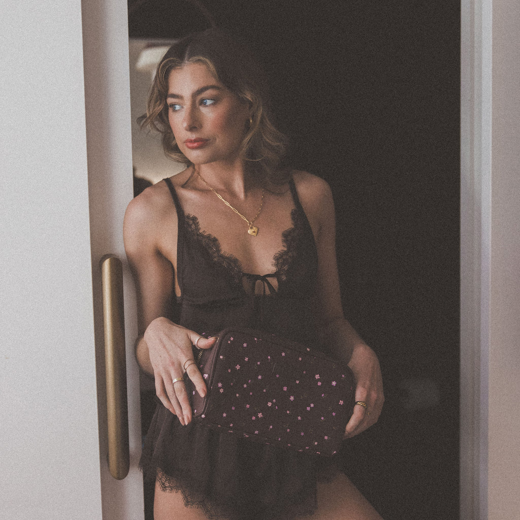 Woman in black lace lingerie holding a clutch, standing in a doorway.