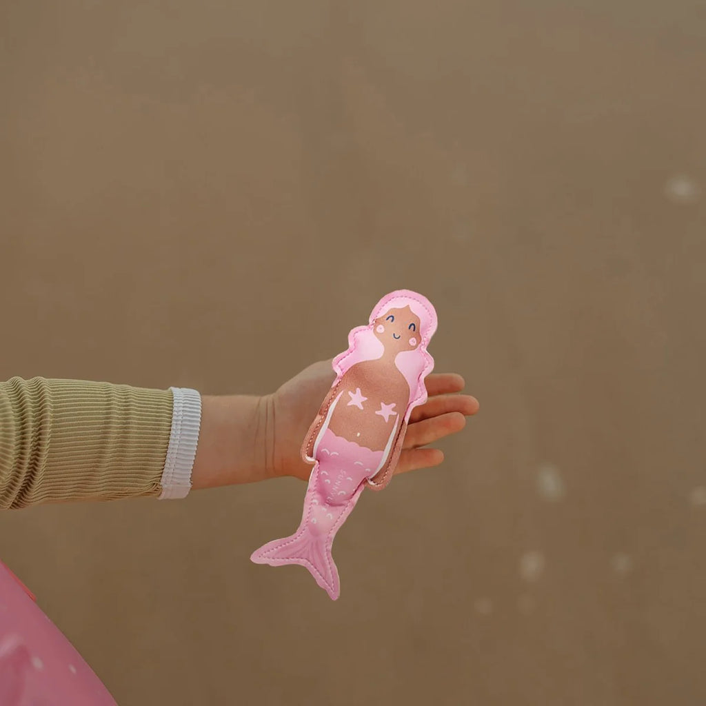 Hand holding a pink mermaid toy against a brown background