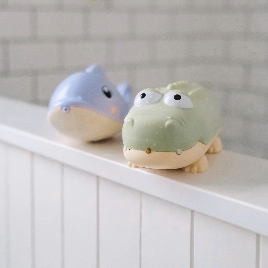 Two cartoonish animal figurines, one green and one blue, on a white surface with a tiled wall background.