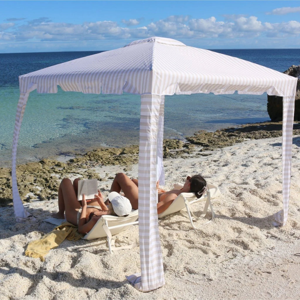 Two people relaxing under a striped beach canopy with ocean view
