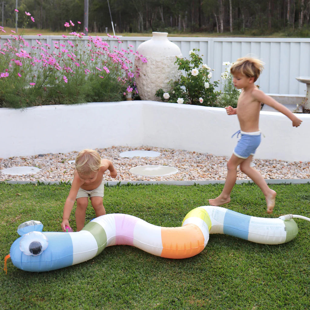 Two children playing with a colorful inflatable snake toy on grass near a pool.