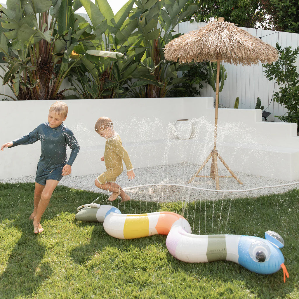 Children playing with a colorful snake-shaped sprinkler in a garden.