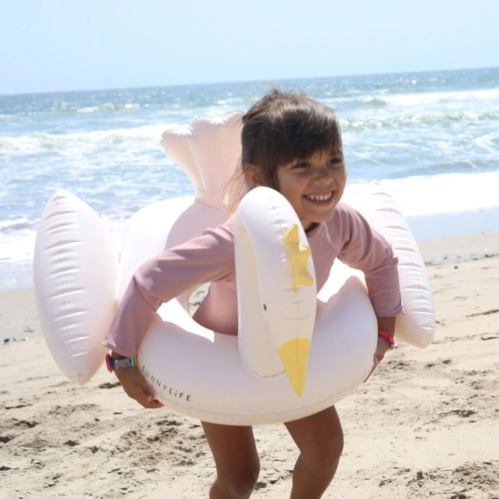 Child holding a swan-shaped inflatable pool toy on a beach