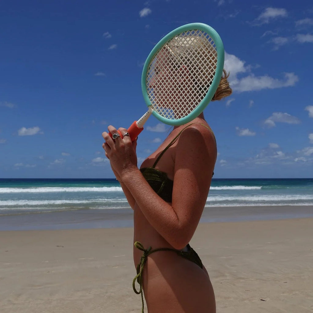 Person on a beach holding a racket with a blue sky and ocean in the background