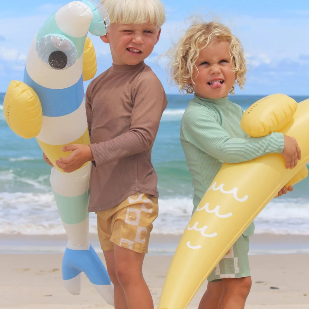 Two children holding inflatable toys on a beach with ocean in the background